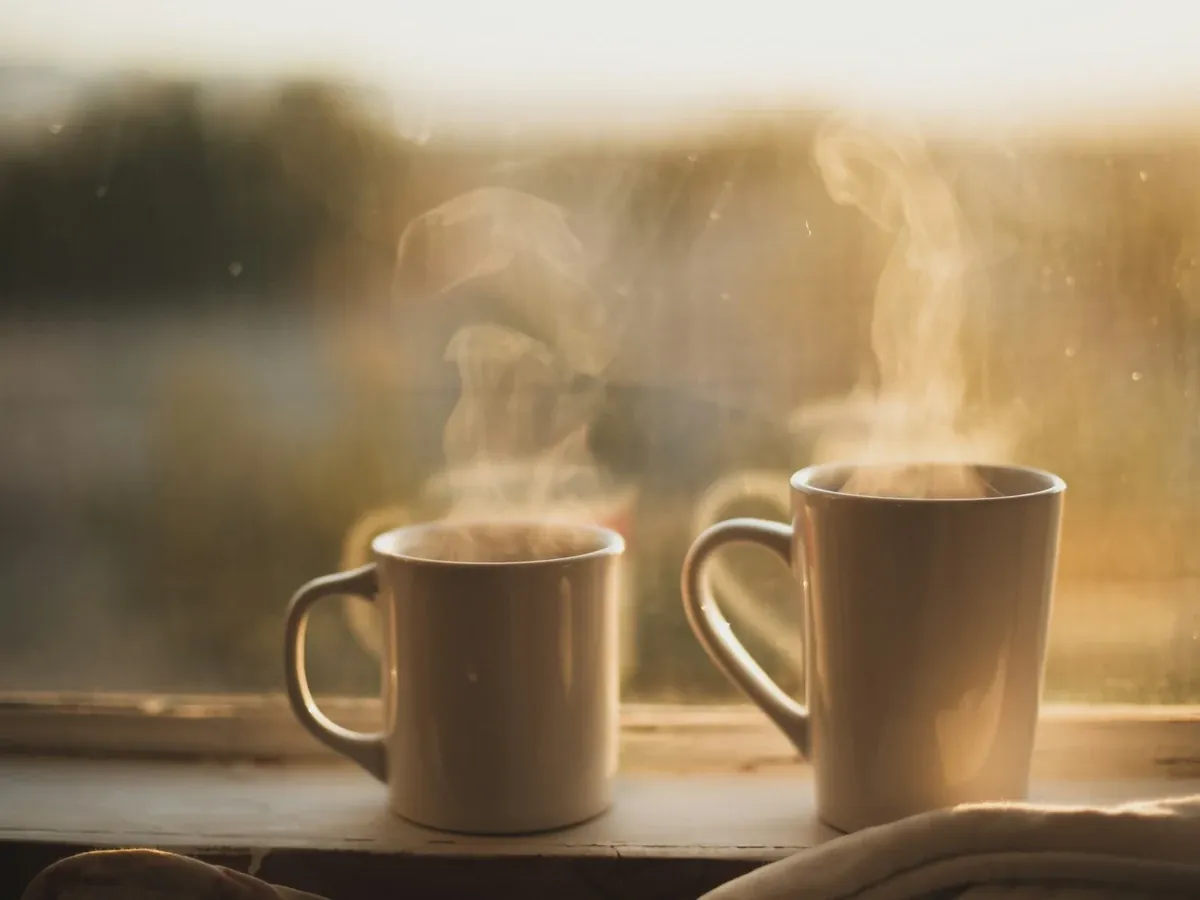 Two steaming mugs on a windowsill in late-afternoon light